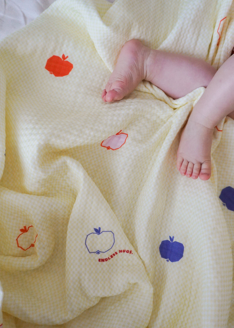 Żółty kocyk bawełniany Endless Hugs z motywem kolorowych jabłek w różnych odcieniach.