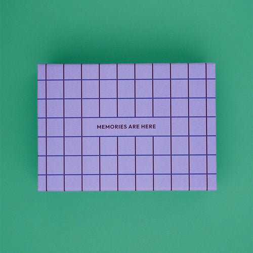 Erinnerungskiste – Erinnerungsbox für Babys im Karomuster - Lila von Endless Hugs mit der Aufschrift „MEMORIES ARE Here“ auf dem Deckel ist das ideale Geschenk für Eltern, um Erinnerungen aus dem ersten Lebensjahr zu bewahren. Gezeigt auf grünem Hintergrund.