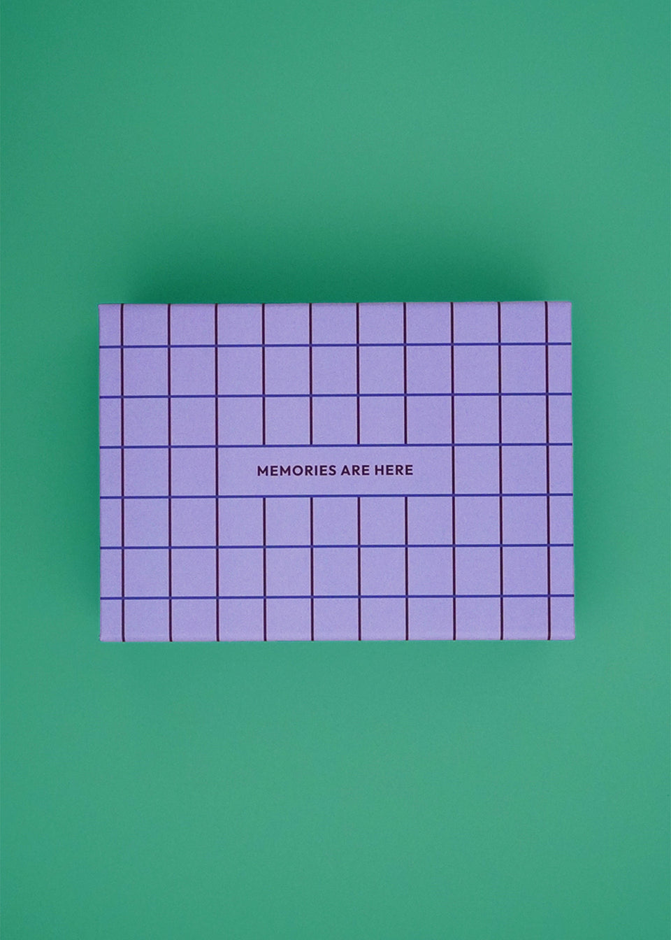 Pudełko Pamięci – Pudełko wspomnień dla niemowląt w kratę - Lila by Endless Hugs z napisem „MEMORIES ARE Here” na wieczku to idealny prezent dla rodziców na wspomnienia z pierwszego roku życia. Pokazane na zielonym tle.