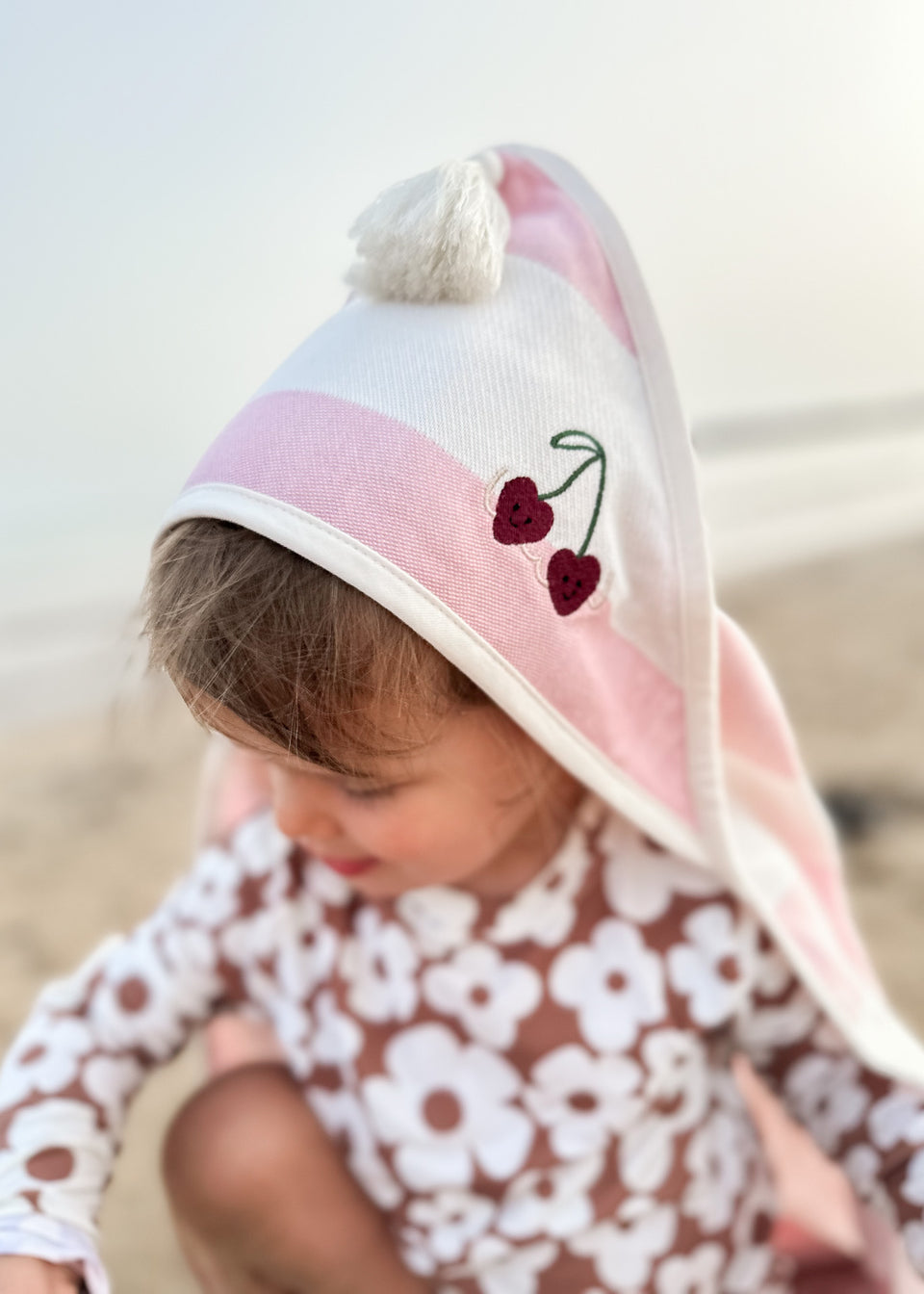 Dziecko w stroju z kwiatowym wzorem cieszy się plażą, owinięte w Endless Hugs Ręcznik Dla Niemowlaka Z Kapturkiem, bambusowy ręcznik z wzorem wiśni.