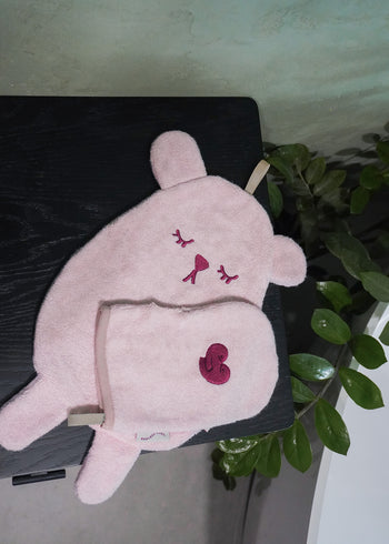 RĘCZNICZEK BAMBUSOWY BEAR, różowy dywanik łazienkowy w kształcie misia i pasująca do niego myjka marki Endless Hugs, wykonane z frotte bambusowej, przedstawione są na ciemnej powierzchni z zielonymi liśćmi.