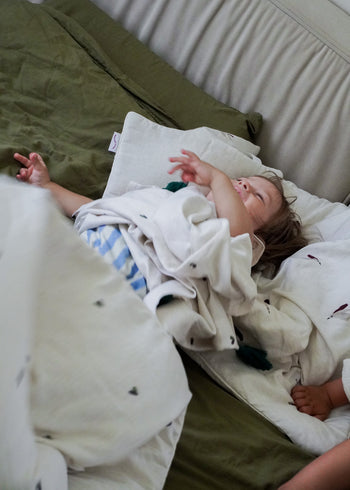 Maluch śpi spokojnie na łóżeczku, częściowo przykryty białym kocykiem, otoczony zielonymi prześcieradłami z bambusowego otulacza Endless Hugs o nazwie OTULACZ DLA NOWORODKA - BAMBUSOWY 100x100 CM / SERDUSZKA o właściwościach hipoalergicznych.