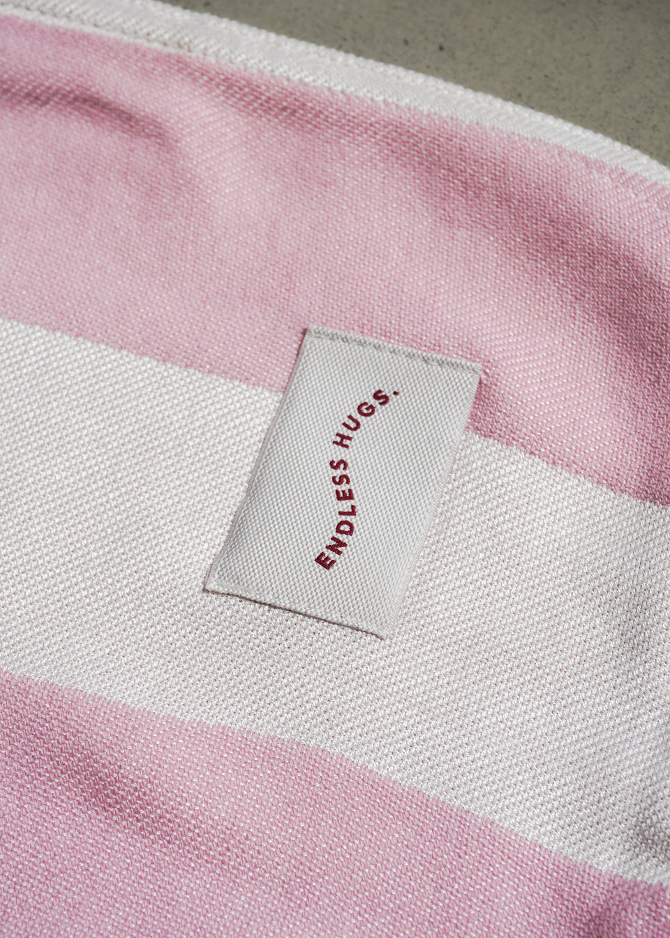 Nahaufnahme eines gemütlichen rosa-weißen gestreiften Stoffes von Endless Hugs, hergestellt aus weicher Bambusviskose. Dieses Material, genannt PONCHO AUS BAMBUS IN ROSA STREIFEN / KIRSCHEN, eignet sich perfekt zur Herstellung einer Badehaube, die ideale Wärme und Komfort bietet.