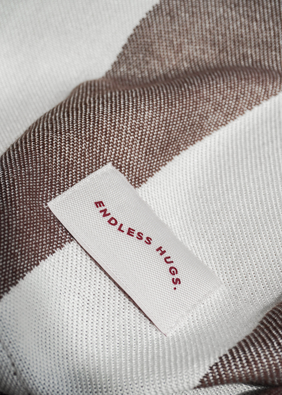 Zbliżenie na tkaninę wiskozową bambusową w brązowe paski z metką „Endless Hugs” z produktu „Ponczo z Bambusa w Brązowe Pasy/Serduszko” oferującego niezrównany komfort.
