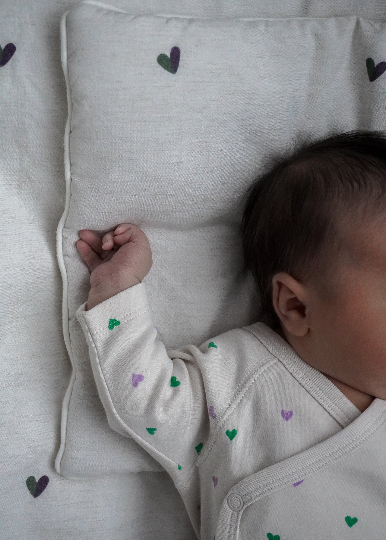 Niemowlę śpi na POŚCIELU DZIECIĘCA - BAMBUSOWA / SERDUSZKA firmy Endless Hugs, ubrane w lekki strój z zielonymi i fioletowymi serduszkami. Pościel bambusowa, znana z hipoalergicznych i termoregulujących tkanin, wzmacnia spokojny sen.