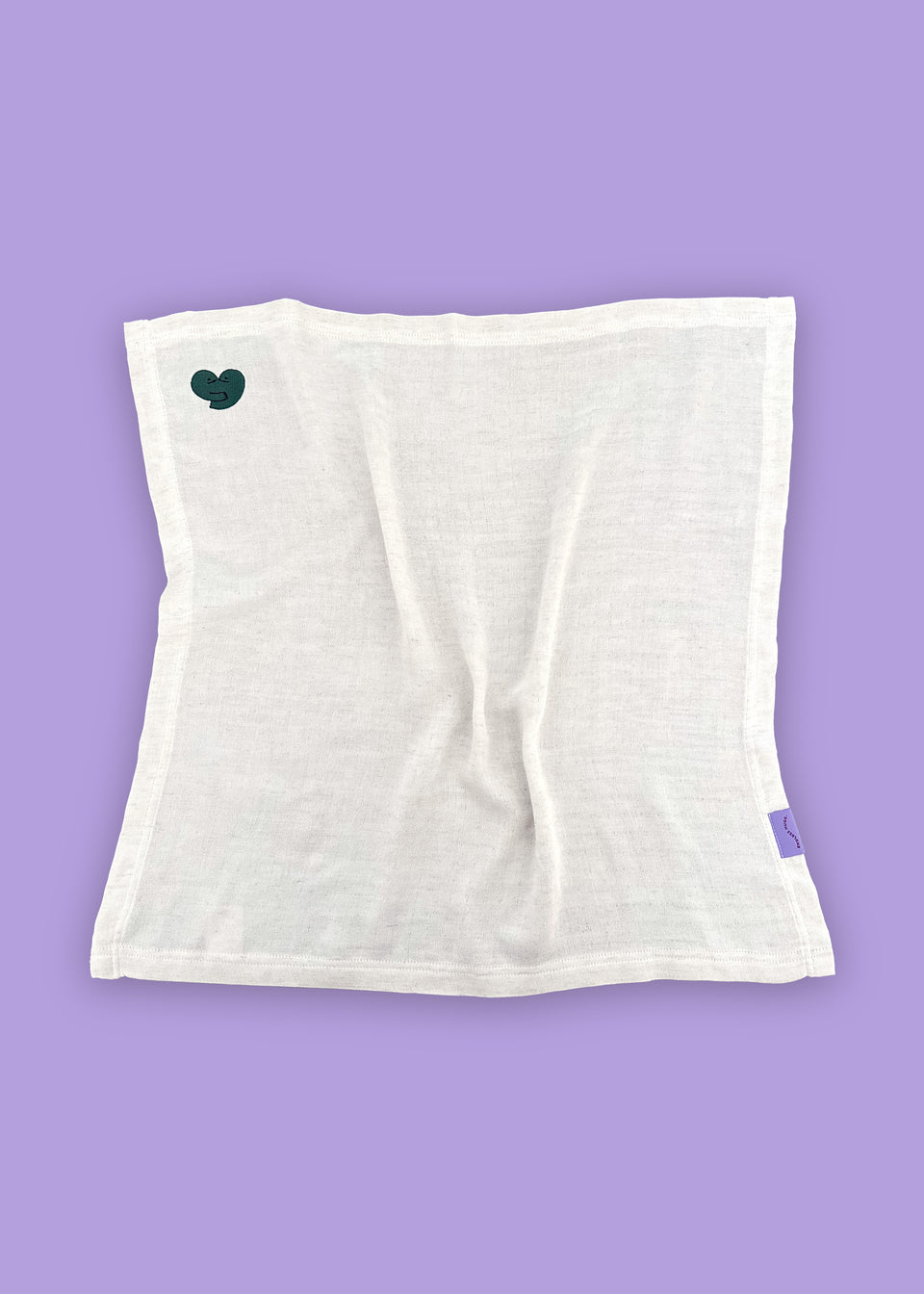 Biała tkanina od Endless Hugs, wykonana z tkaniny bambusowej, z małym zielonym serduszkiem, rozłożona płasko na fioletowym tle. Produkt: PIELUSZKI MUŚLINOWE Z BAMBUSA - DWUPAK 60x60 CM / SERDUSZKA.