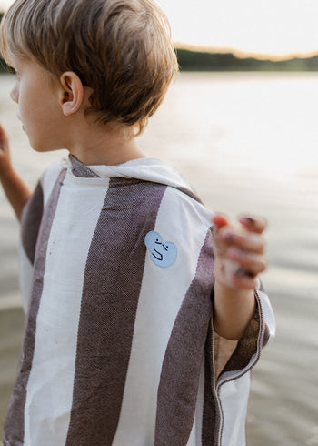 Bawełniane ponczo dziecięce Endless Hugs w brązowe paski z naszywką, idealne na plażę.